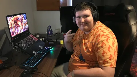 Jesse with headphones & laptop computer looking at camera, hand doing V for victory