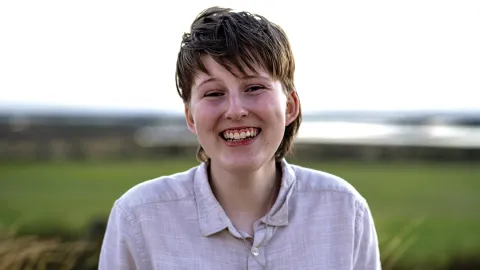 young man smiling at the camera - background is out-of-focus grass (probably)