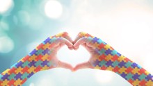 Hamds making heart shape - with autism puzzle-pieces imagery superimposed on skin of arms